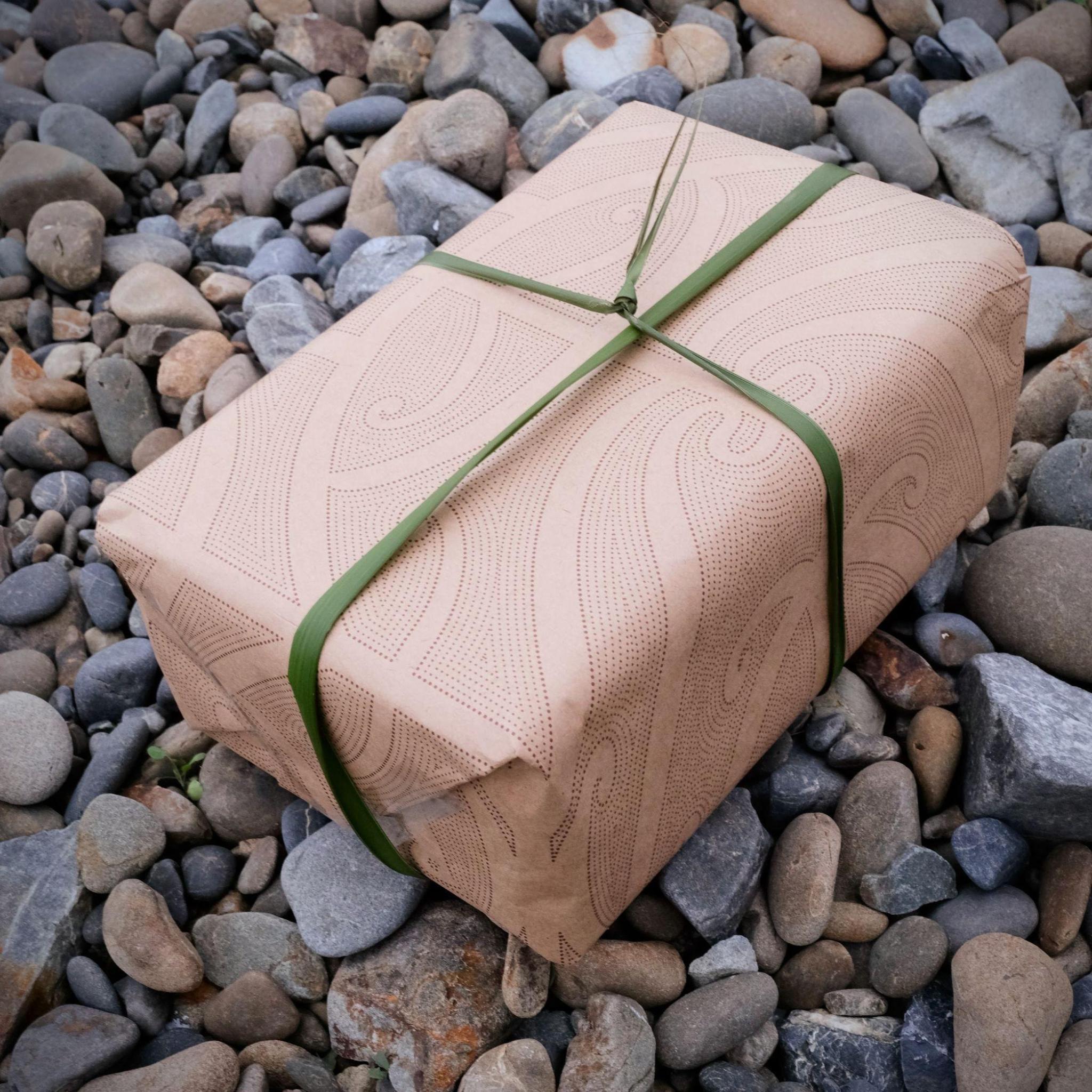 Māori wrapping paper with Harakeke flax ribbon on pebbles